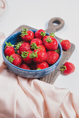 Ripe strawberries in blue bowl on rustic wooden board, elegant style, sweet berry for summer dessert. Filled bowl or plate by red fresh strawberries. Seasonal harvest. Elegant strawberry background