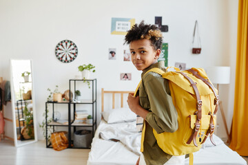 Wall Mural - Waist up portrait of mixed-race teenage boy holding backpack and smiling at camera while getting ready for school, copy space