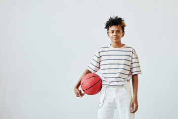 Wall Mural - Minimal portrait of mixed-race teenage boy holding basketball ball while standing against white background, copy space