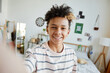 © Seventyfour - POV of mixed-race teenage boy smiling at camera during video chat or live stream in cozy room, copy space