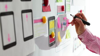 A designer is developing a web application for mobile phones on a white board. A woman draws a sketch of the interface for a smartphone. User experience.