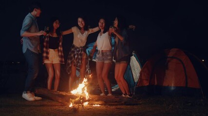 Wall Mural - Group of Asia best friends teenagers dancing and drinking have fun salute toast of bottle beer enjoy party with happy moments together in campsite at night. Beautiful bonfire camping traveller concept