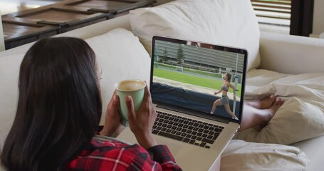 Sticker - Composite of woman sitting at home holding coffee watching athletics high jump event on laptop