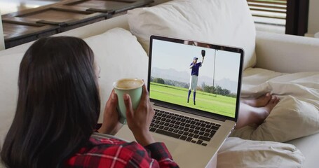 Wall Mural - Composite of woman sitting at home holding coffee watching baseball game on laptop