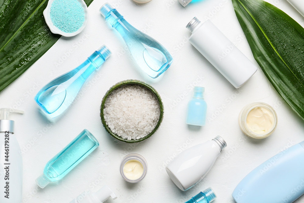 Different cosmetic products and sea salt on light background