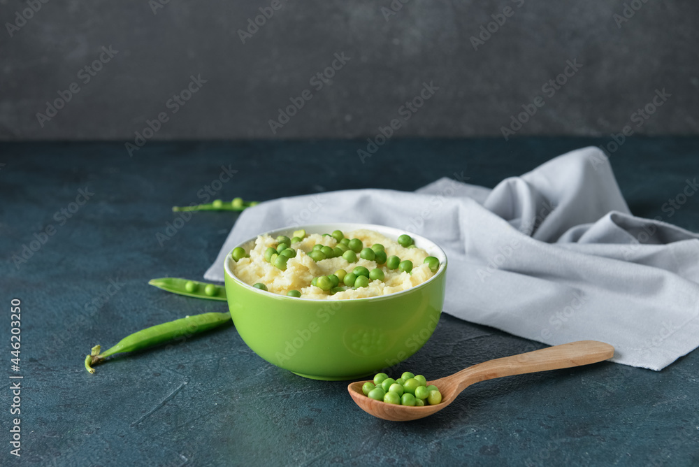 Bowl with mashed potatoes, green peas and spoon on color background