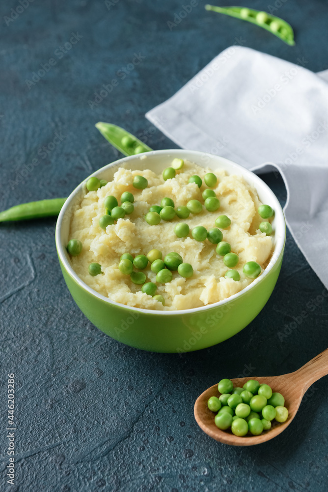 Bowl with mashed potatoes, green peas and spoon on color background