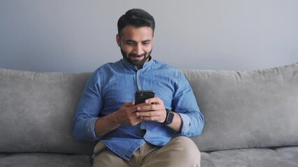 Happy smiling millennial indian man in causal jeans shirt using mobile app