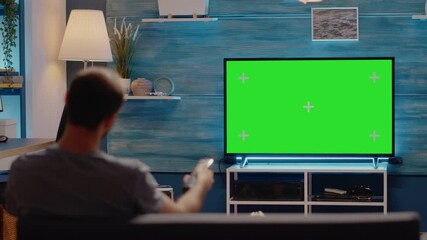 Caucasian man switching channels on green screen television display in living room. Copy space media with chroma key background used for blank mockup template and digital isolated design