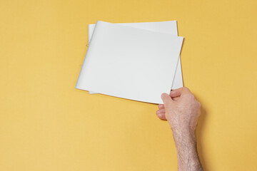 Poster - Male hand touching a catalog with blank cover on yellow background, mock-up series template