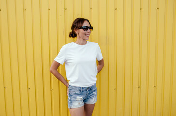 Wall Mural - Young smiling pretty happy cheerful positive woman in blank white t-shirt near color background on street. Mockup for design.