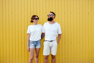 Wall Mural - Young smiling pretty happy cheerful positive couple in blank white t-shirts near color background on street. Mockup for design.