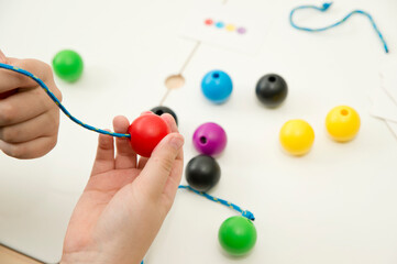 Primary Lacing Beads - Educational Toy With Wooden Balls. Colourfull rainbow wooden lacing toy for toddlers. Threading toy for fine motor skills development. Boy holding ball with lace