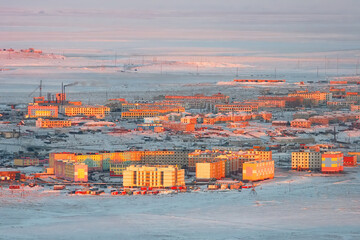 Wall Mural - Winter aerial view of an arctic settlement in the snowy tundra. Top view of buildings illuminated by the sun at sunrise. Urban-type settlement Ugolnye Kopi, Chukotka, Siberia, Far East of Russia.