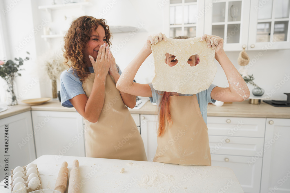 Mother and daughter having fun while cooking dough in kitchen - obrazy, fototapety, plakaty 