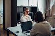 © exebiche - Two young adult women sitting at table facing each other, working on laptops in the home interior. Focus on face of blonde with glasses. Freelance, coworking, remote work, self-employment.