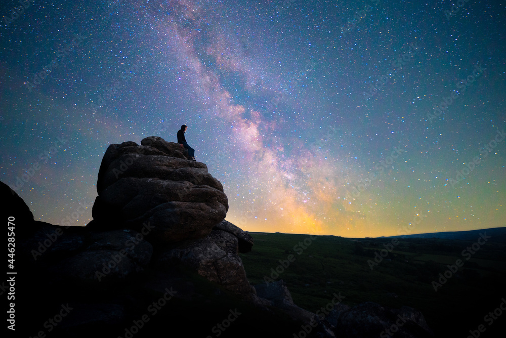 Figure stargazing atop rocks beneath the Milky Way, Dartmoor National Park, UK - obrazy, fototapety, plakaty 