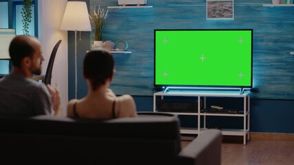 Green screen on television at home in living room used by young man and woman for copy space design of chroma key and modern equipment. People with isolated template for mockup background