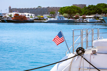 The Flag Of The United States Flutters In The Wind On A Steel Flagpole At The Stern Of A Motor Yacht. Marina In The Port City At Summer. Mediterranean Coast Of Greece, Dodecanese, Rhodes Island.
