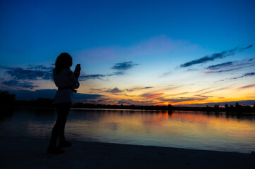 Wall Mural - silhouette of a girl with a phone on the background of sunset by the lake