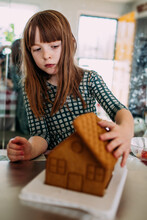 Young Girl Building A Gingerbread House Inside On A Sunny Day
