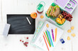 Top down view of an assortment of school supplies and lunch along with a blank chalkboard, chalk and eraser.