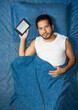 © Narayan - young latin man reading an e-reader book on blue bed, electronic e-book concept