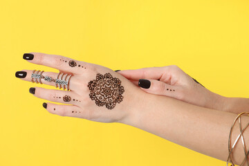 Wall Mural - Woman with henna tattoos on hands against yellow background, closeup. Traditional mehndi ornament