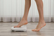 Woman stepping on floor scales indoors, closeup. Weight control