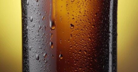 Wall Mural - Beer drop slowly trickles down the misted beer bottle, following the camera. Yellow background. 