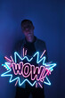 A handsome guy is holding a neon wow sign in pink and blue. Trendy style. WOW. Neon sign. Custom neon. Home decor.