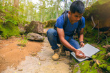 Fototapeta  - Biologist or botanist recording information about small tropical plants in forest. The concept of hiking to study and research botanical gardens by searching for information.