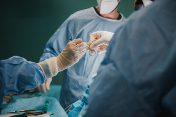 Wall Mural - Medical surgeon team operating patient in surgical room at private clinic - Focus on right hand holding suture scissor