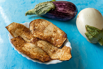 Eggplants battered and fried in oil, on a blue wooden background and with two aubergines adorning the composition.