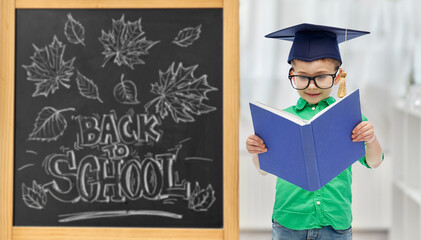 education, learning and people concept - happy little student boy in bachelor hat or mortarboard and eyeglasses over chalkboard with back to school lettering on background