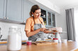© Syda Productions - culinary, baking and cooking food concept - happy smiling young woman making layer cake and spreading topping cream on kitchen at home