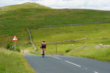 Cycling Along A Scenic Country Road, A Man Is Facing A Big Hill Ahead Of Him As He Makes His Way Along The Road In The Yorkshire Dales, North Yorkshire, England, UK.