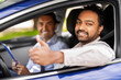 © Syda Productions - driver courses, exam and people concept - happy smiling indian man showing thumbs up and driving school instructor with clipboard in car