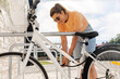 © Syda Productions - people, leisure and lifestyle - happy young woman parking her bicycle and fastening lock on city street