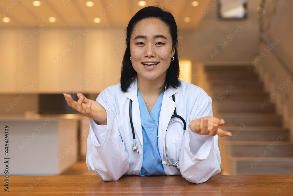 Portrait of asian female doctor sitting at desk talking during video consultation - obrazy, fototapety, plakaty 