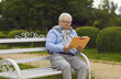 © Studio Romantic - Elderly senior man wearing eyeglasses enjoy reading book sitting on wooden bench in city public park outside. Happy retirement lifestyle, hobby and pleasure. Concept of serene old age