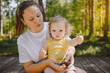 © Алина Троева - Little cute baby toddler girl blonde with curls on mother's arms. Mother and daughter playing spend time together outdoors at countryside front yard summertime. Healthy happy family childhood concept