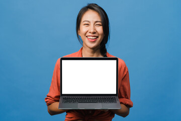 Young Asia lady show empty laptop screen with positive expression, smiles broadly, dressed in casual clothing feeling happiness isolated on blue background. Computer with white screen in female hand.