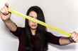 © AliciaFdez - Brunette young woman with long hair holding a yellow measuring tape on a white background