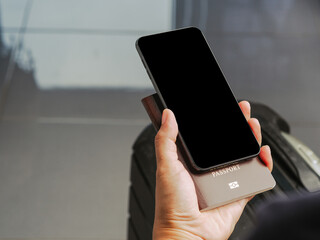 Wall Mural - hand holding of a smartphone with suitcase background. close-up photo. space for text. technology an