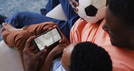 Canvas Print - Composite of father and son at home watching basketball game on smartphone