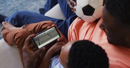 Sticker - Composite of father and son at home watching athletics long jump event on smartphone