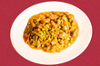 A white plate of vegetable stew with legumes such as peas, carrots, abas and chorizo on a red tablecloth.