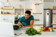 © Astarot - Happy African American man cooking healthy dinner at home. He is following a video tutorial on the laptop.
