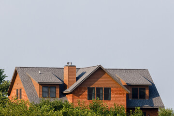 top half of a 2 story home surrounded by trees and leaves with blue sky above for copy space.